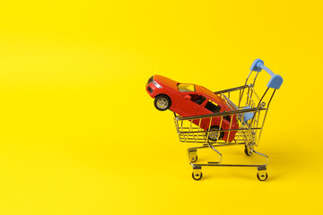 Buying car concept. Shopping cart with toy car model on yellow background