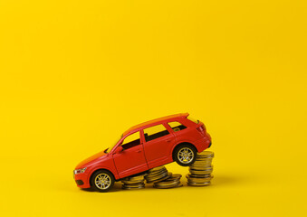 Toy red car model with a stack of coins on a yellow background. Saving money, investing, buying car concept