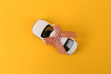 Toy auto model rewound gift ribbon with bow on yellow background. Car as gift, surprise