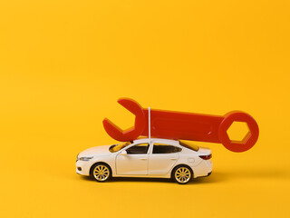 Toy car model with a wrench on a yellow background. Auto service, repair concept