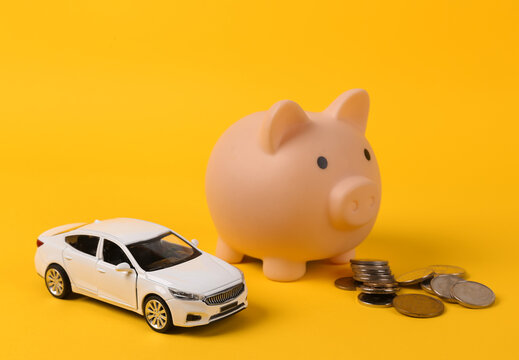 Toy car model with a stack of coins and piggy bank on a yellow background. Saving money, investing, buying car concept