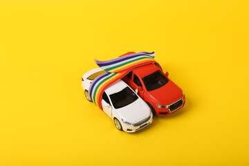 Two toy car models wrapped in rainbow lgbt tape on yellow background