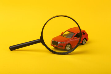 Toy car model through magnifying glass on yellow background