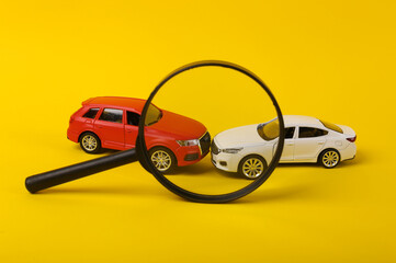 Two mini toy car crash through magnifying glass on yellow background, incident, car traffic accident