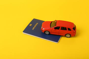 Toy car model with a passport on a yellow background. Travel concept