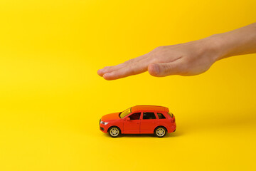 Auto protection concept, insurance. Hand over toy car model on yellow background