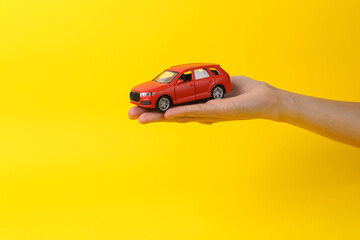 Toy car on the palm of a woman's hand on a yellow background. Protection, insurance auto concept