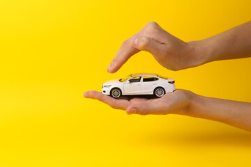 Fototapeta premium Female hands with a toy car and cover it from above on a yellow background. Protection, insurance auto concept
