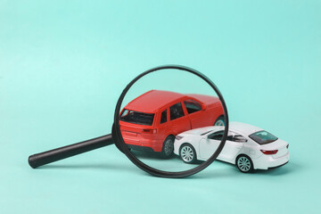 Two mini toy car crash through magnifying glass on blue background, incident, car traffic accident