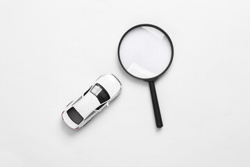 Toy car model and magnifying glass on white background