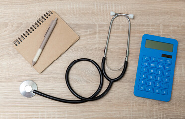 Medical stethoscope with notebook and calculator on wooden table