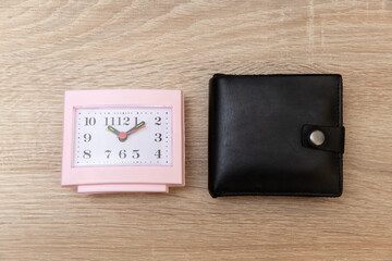 Alarm clock and leather wallet on a wooden table