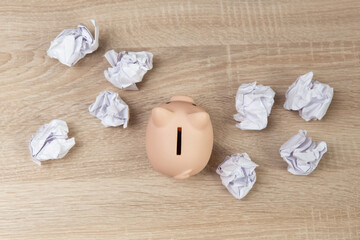 Piggy bank among crumpled sheets of paper on wooden table. Business concept