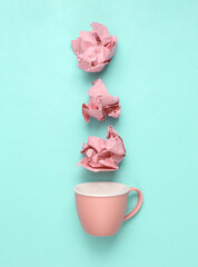 Pink crumpled sheet of paper with cup on blue background. Minimal still life