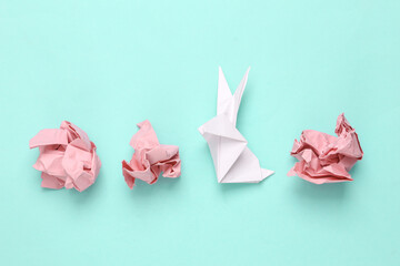 Crumpled pink paper with origami rabbit on a blue background. Easter symbol