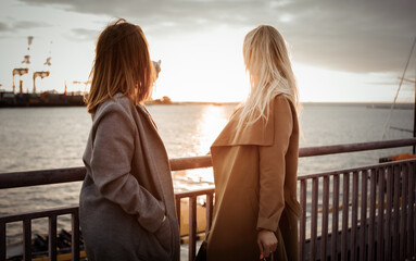 Two attractive women girlfriends in autumn coats at sunrise at the sea