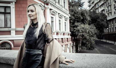 Cute attractive fashion woman in autumn coat posing against the background of urban architecture. Street fashion