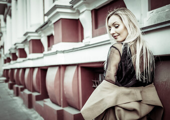 Cute attractive fashion woman in autumn coat posing against the background of urban architecture. Street fashion