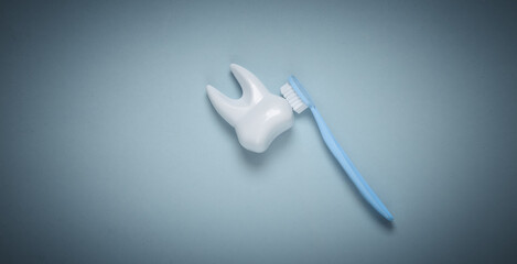 Toothbrush cleans toy plastic tooth on blue background. Dental care concept