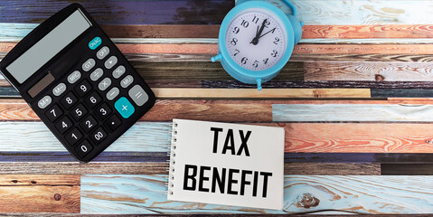 On a notepad the inscription TAX BENEFITS on a striped background with a calculator and a clock.