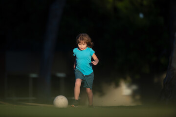 Child playing football on the playground in park. Boy child kicking football on the sports field during.