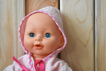 portrait of a toy doll in a pink bathrobe on a wooden background