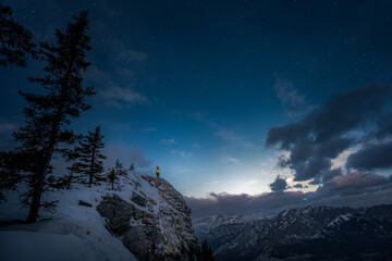 A female hiker in a yellow jacket standing at the edge of the mountain observing the sunrise and...