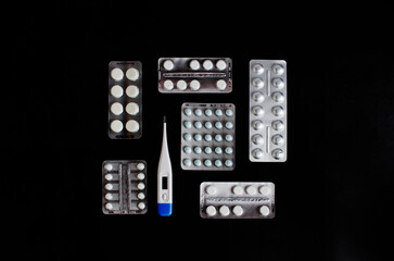 Blisters with pills and an electronic thermometer on a black background. High quality photo