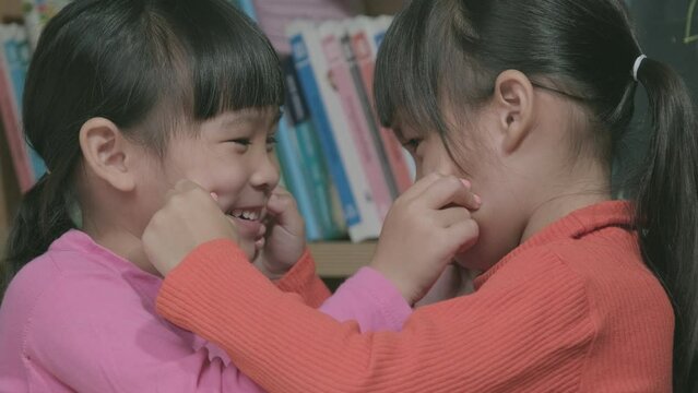 Asian sisters touch each other's cheeks and smile face to face. two cute little girls playing together at home. Lovey family spending time together indoors.