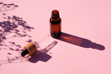 Open bottle with dropper pipette with serum or essential oil. Pink background with daylight....