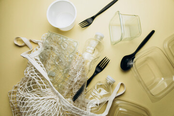 different household plastic products top view on a beige background. plastic trash in a reusable rag bag. sorting plastic. a disposable plastic item and a reusable bag.