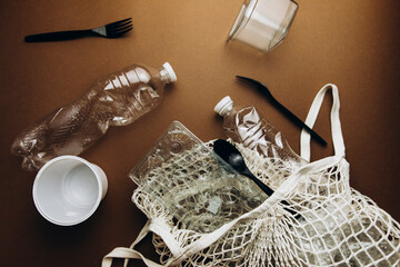 used plastic things top view on a brown background. plastic trash in a reusable rag bag. sorting plastic. disposable plastic and reusable bag.