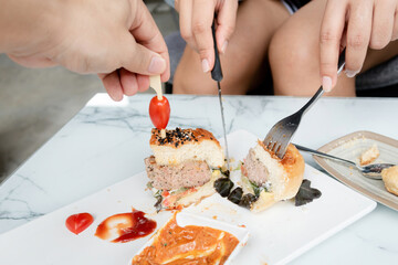 Obraz na płótnie Canvas Two people hand cutting a hamburger on a plate