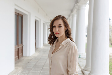 pretty caucasian young woman in beige blouse, seductive red lipstick and wavy hair standing on...