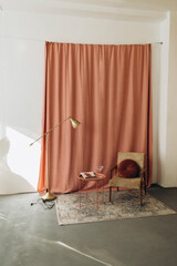 an example of a stylish photo zone in a photo studio. an old armchair with a pillow near a coral curtain. loft style room details with high ceilings and vintage furniture.
