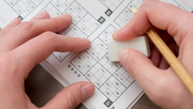 A woman's hand erases a number in Sudoku with an eraser.Tasks and puzzles for the development of logic and intelligence. Classes at home and on the road.