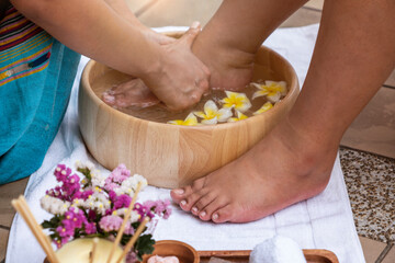 Obraz na płótnie Canvas Feet, young women wash their feet in a wooden tub with frangipani flowers for a foot spa. 