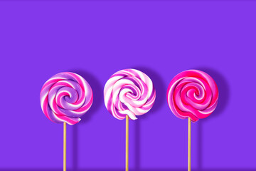 Three colorful baby lollipops on a stick on a purple background, spiral sugar lollipops on a stick, baby sweets, sugar lollipop 