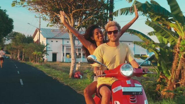 Multiracial happy young couple Caucasian man and Hispanic woman enjoy life vacationing on tropical island riding motor scooter along asphalt road. Interracial friendship, lifestyle, friendship