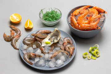 Shrimps on ice on two gray plates. Onion, seaweed and lemon on table.