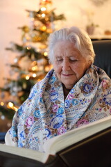 Alte Frau sitz am Weihnachtsbaum und liest