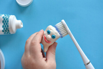 children's hands clean a toy tooth made of plasticine with a toothbrush on a blue background