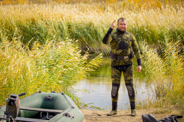 A fisherman in a diving suit stands on the bank of the river with a diving ammunition....