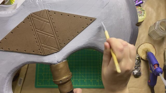 Woman makes viking axe for cosplay festival. Girl draw hatchet with silver paint and brush. DIY celtic weapons in craft workshop.