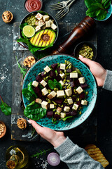 Female hands holding a bowl of beet salad, tofu cheese, spinach and pumpkin seeds. The concept of healthy eating. Top view.