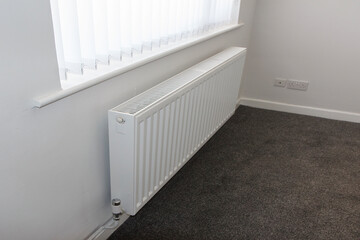Corner of a room with a white radiator and white vertical blinds with a new carpet - house ready...