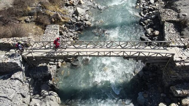 Two people riding mountain bikes on bridge over the Marsyangdi River near Manang Nepal.