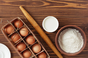 Ingredients for baking - flour, eggs, milk. With rolling pin and pouch. On wooden table
