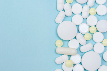 Side border of scattered medical pills on a blue background with copy space.