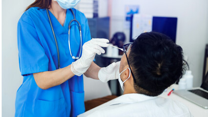 Doctor in a protective suit taking a throat and nasal swab from a patient to test for possible...